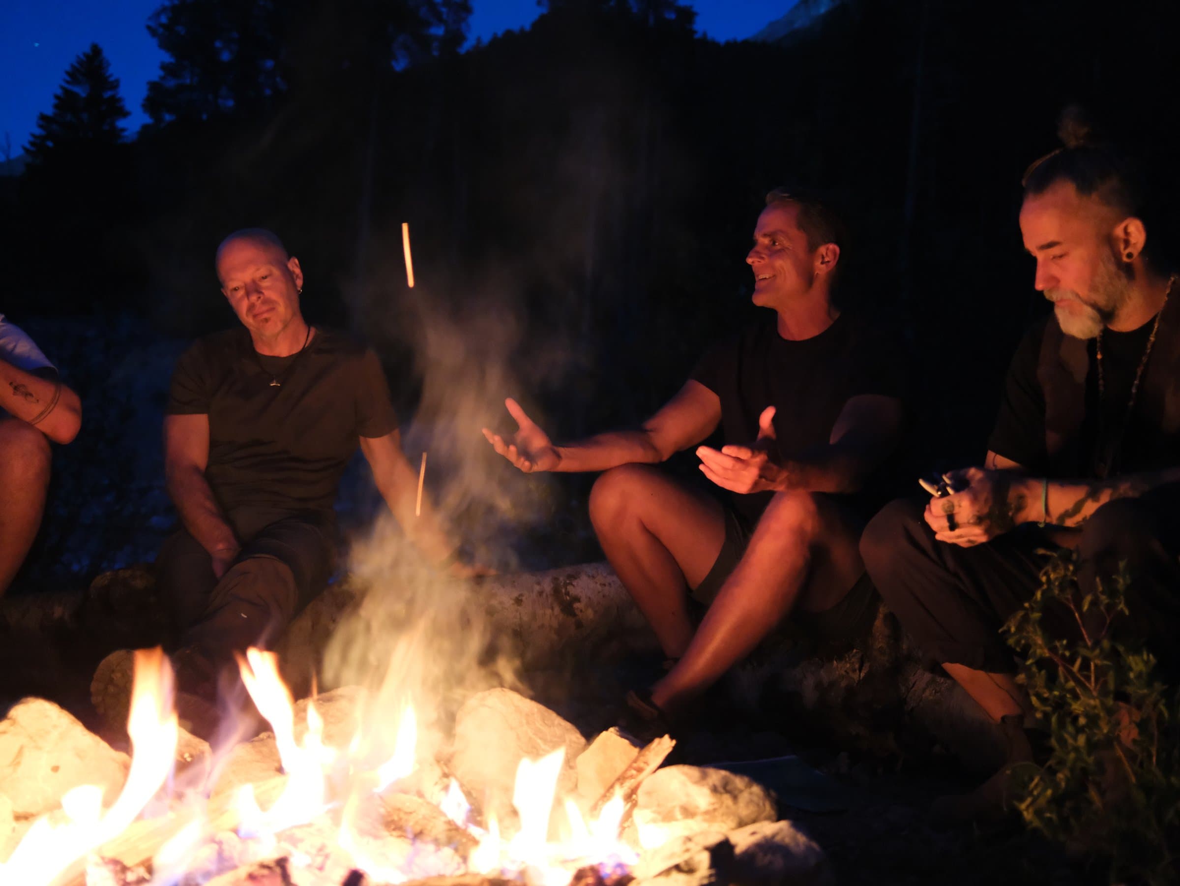 Four men in a fire circle at dusk during a men's retreat in the Swiss Alps