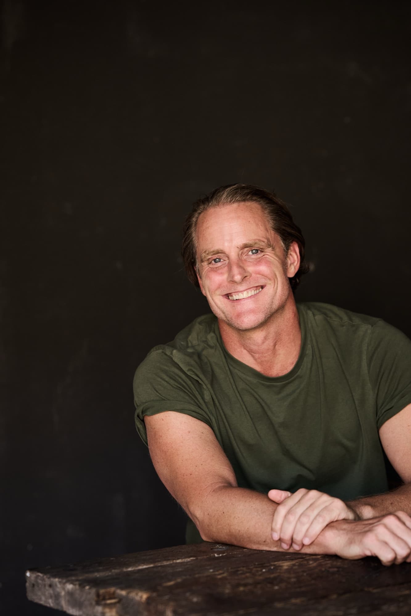 Jason Milne, warm portrait leaning on a wooden table